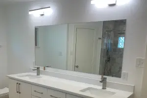 A remodeled shower with a glass door the bath has been tiled and features nickel plated shower head and handles. The remodeled restroom also features a new toilet with shelf.