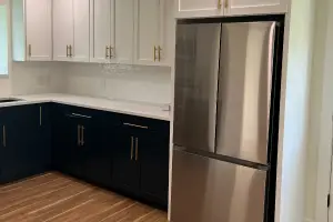 A remodeled kitchen with new fridge, cabinets and counters. The floor has been tiled with light and dark wood patten to accentuate the room.