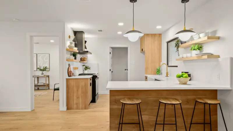 A remodeled kitchen width drop chandelier lights, new kitchen cabinets, shelving, and breakfast bar.